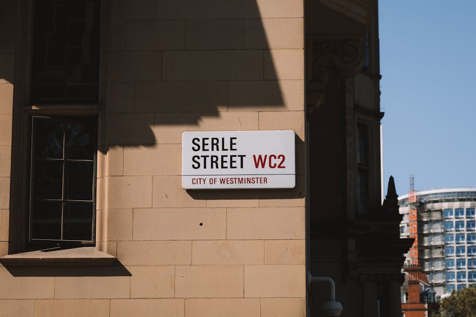 Close-up of a building corner in Maida Vale showing a white and red street sign labeled 'BELL YARD WC2 CITY OF WESTMINSTER,' positioned above a yellow warning sign indicating 24-hour CCTV surveillance